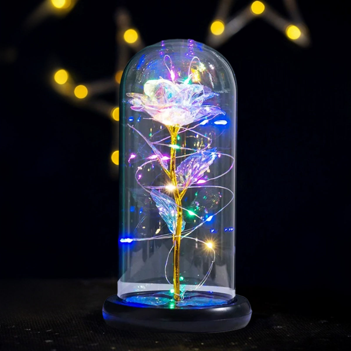 Two red roses glowing under a glass dome with rotating RGB LED colors casting prism reflections on black marble surface, modern party decor concept